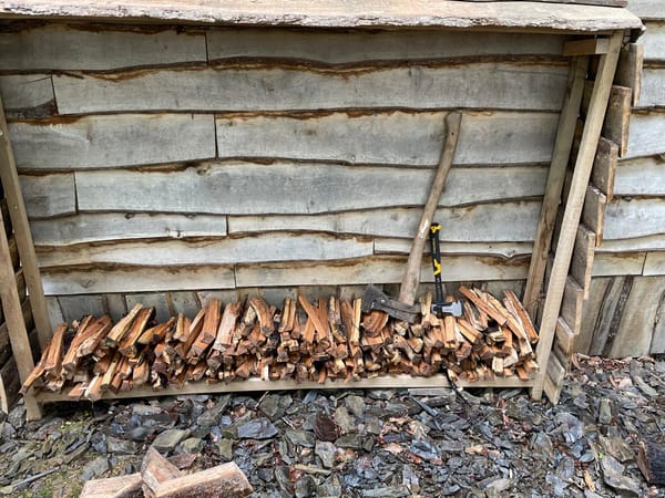 Cabin exterior with timber log shelter and fresh firewood piles in Carmarthenshire